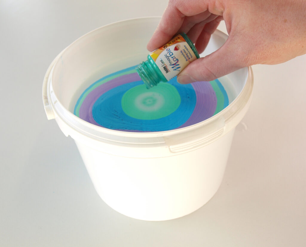 Marmorierfarbe in einen Behälter mit Wasser träufeln.